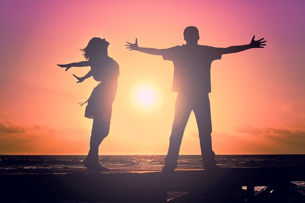 silhouette of woman and man with outsretched arms basking in the sunrise